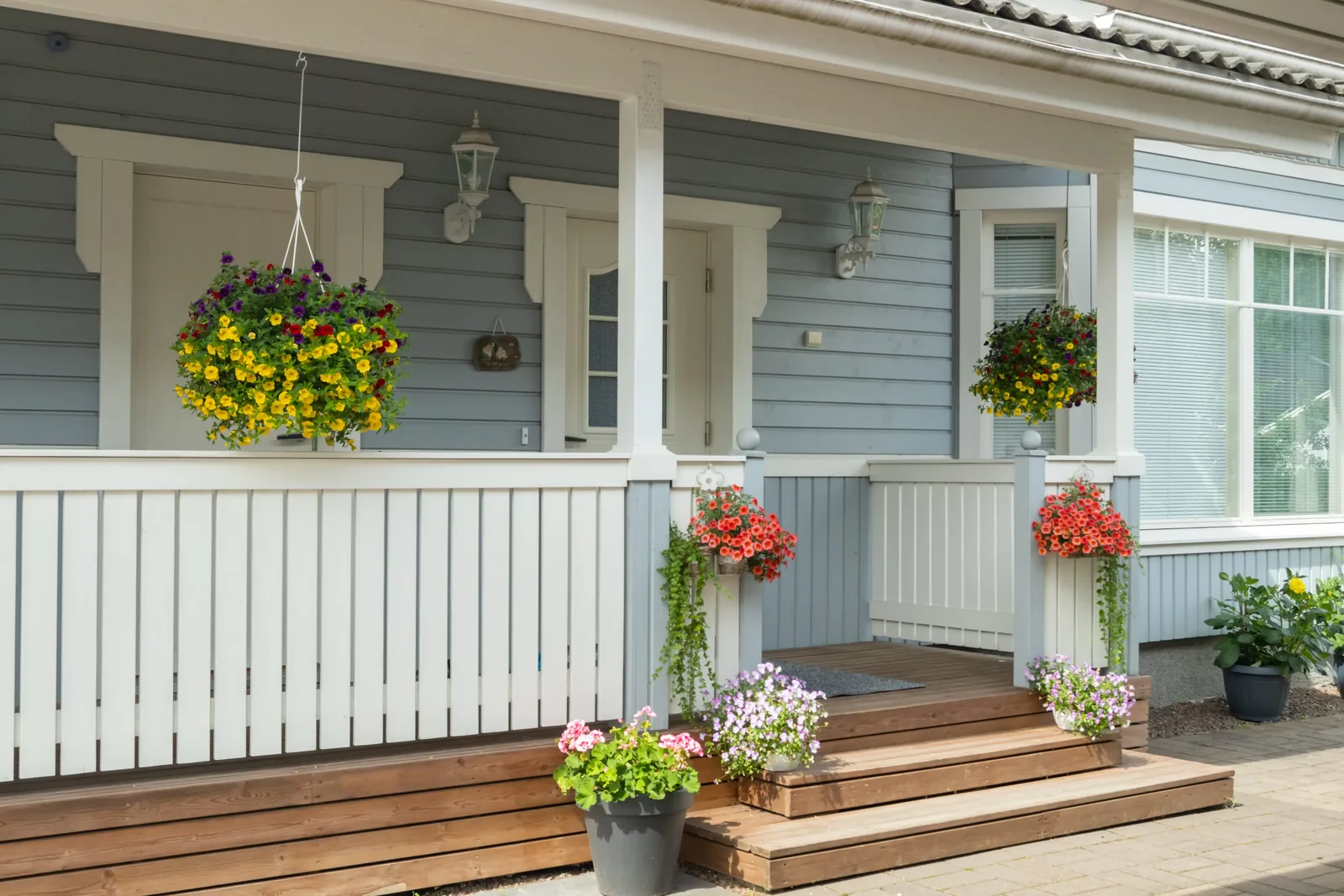 Covered front porch of a light blue home with white railing and hanging flower baskets