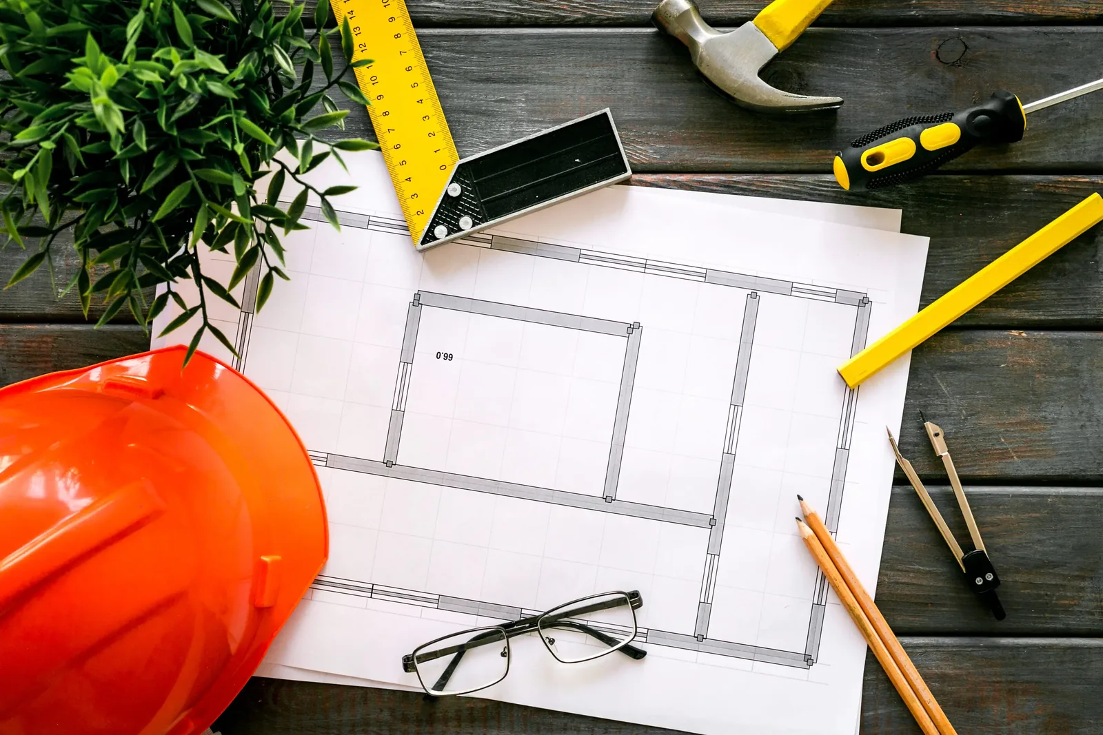 Deck plans on a workbench beside a hard hat, tape measure, hammer and pencil