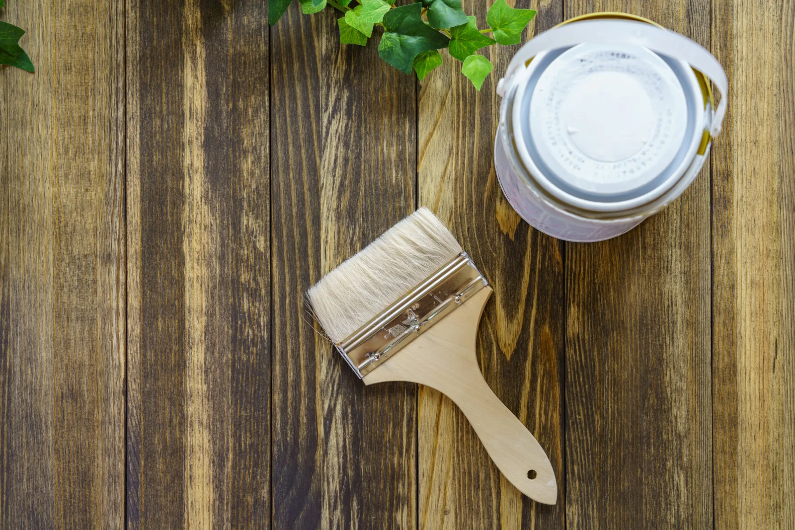 Paint can and brush resting on weathered wood planks