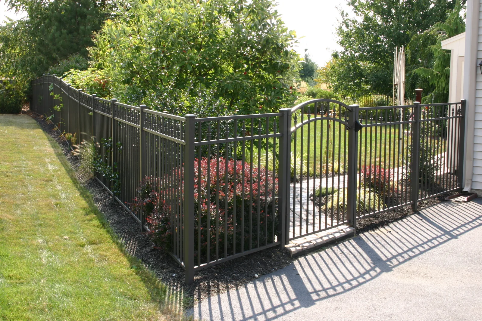 Black aluminum fence and gate enclosing a landscaped bed beside a driveway