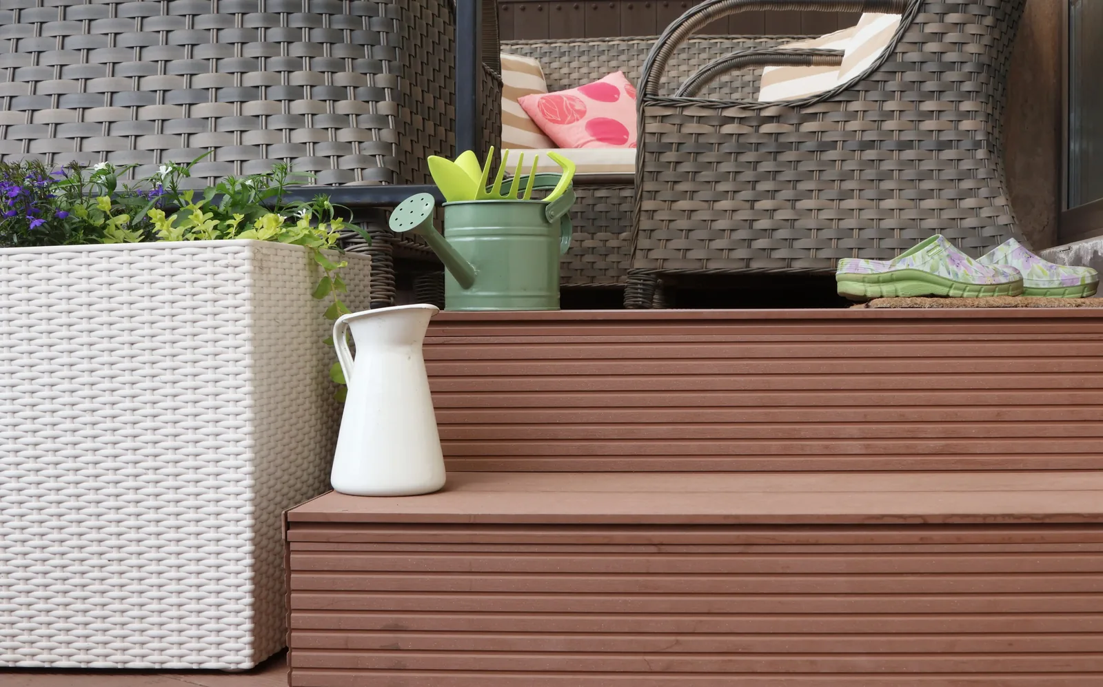 Composite deck step with a white planter, watering can and wicker furniture
