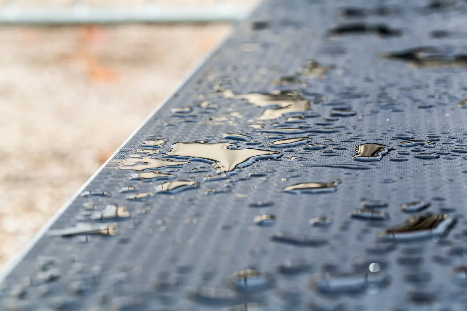 Water beading on the surface of a dark composite deck board