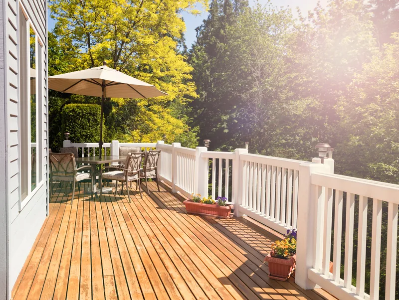 Wood deck with white railing, a table with an umbrella and potted plants
