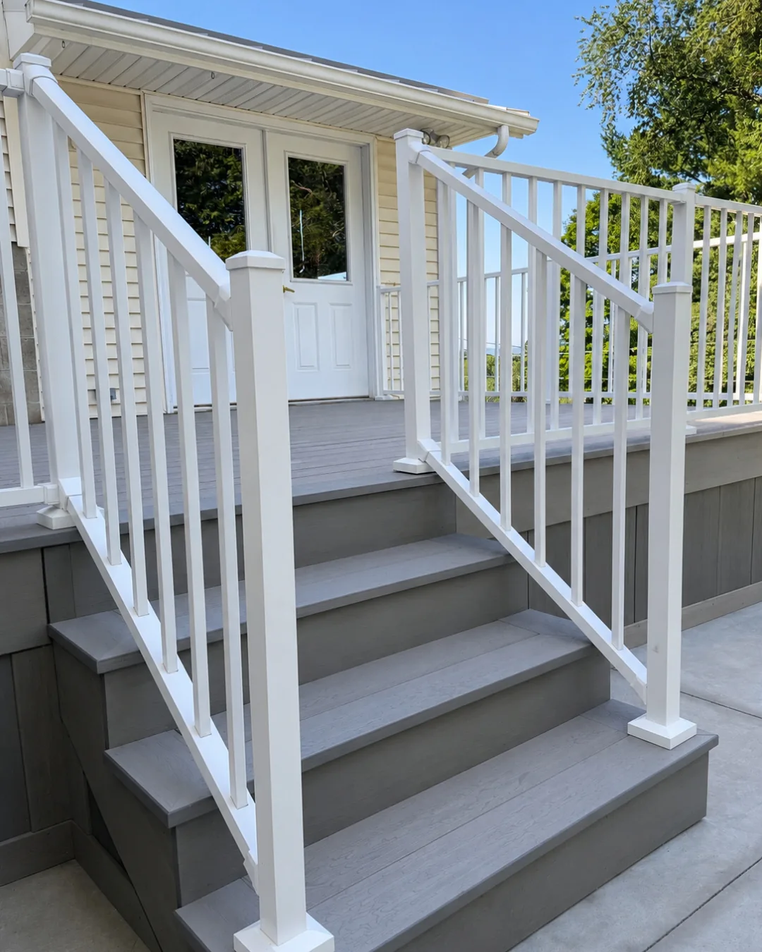 Deck stairs with gray composite treads and white aluminum railing leading up to French doors