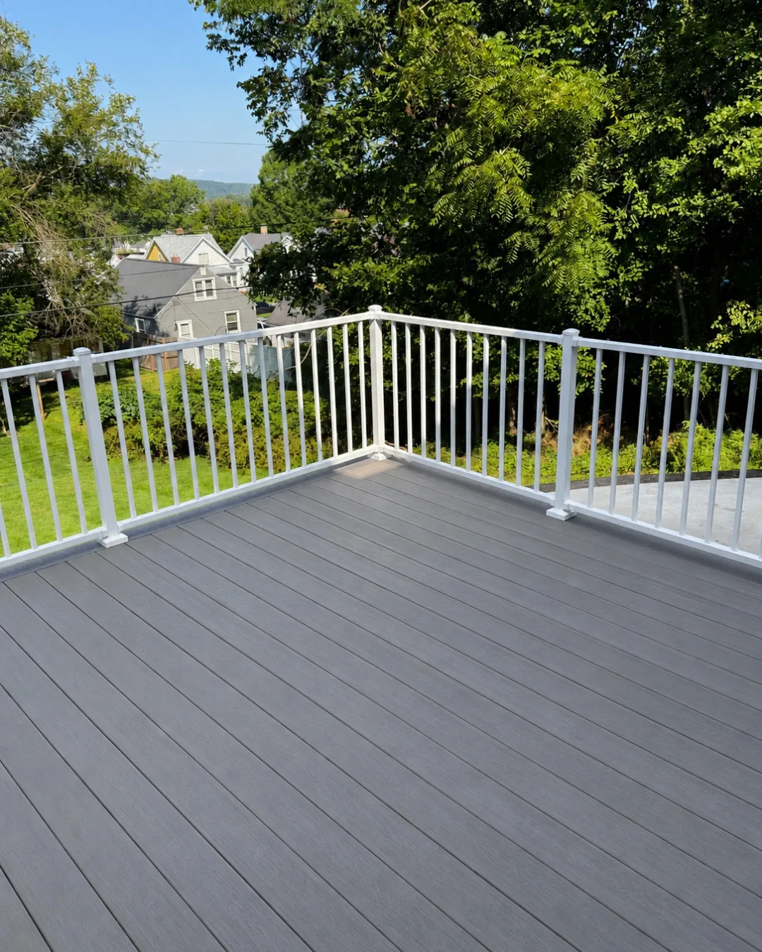 Gray composite deck with white aluminum railing overlooking a wooded backyard