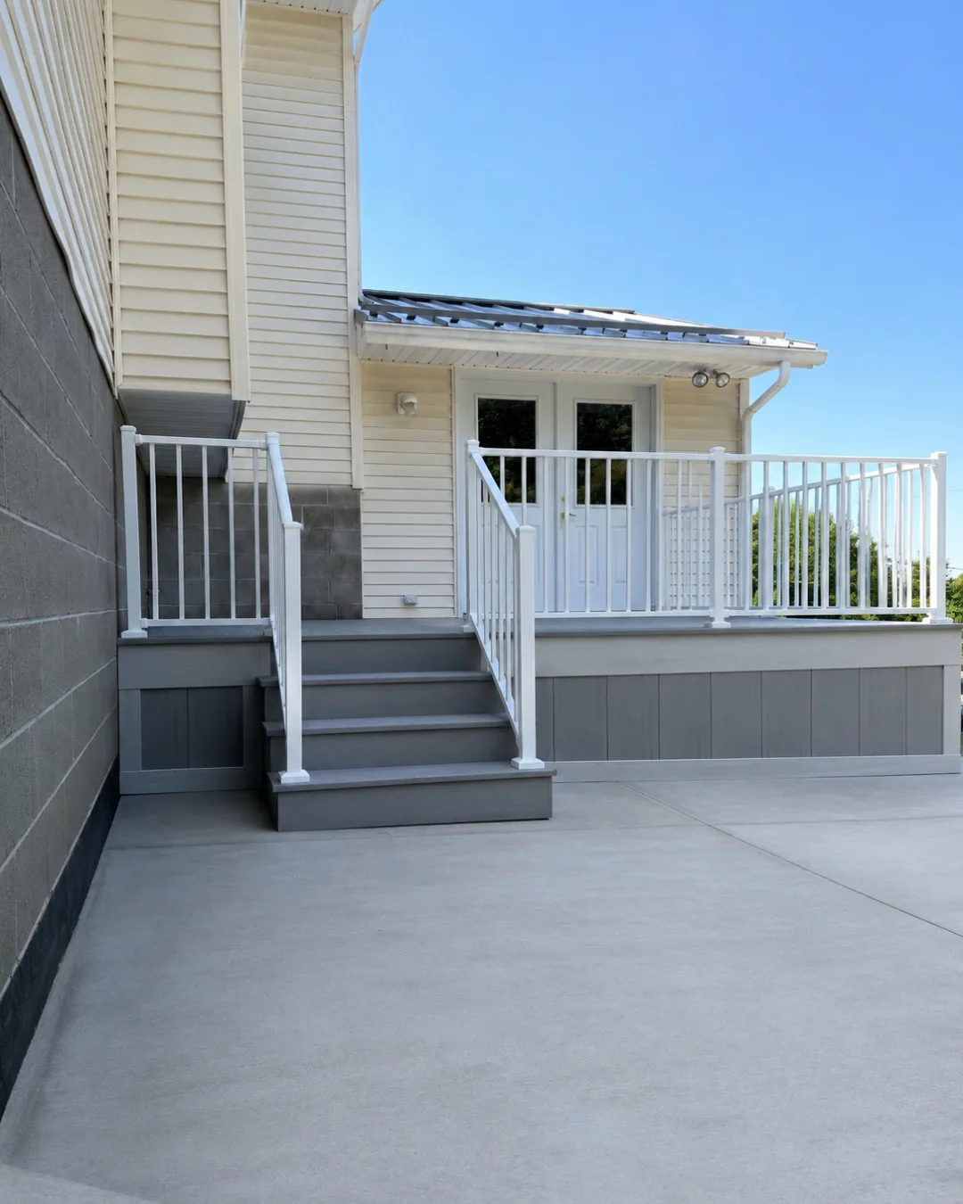Gray composite deck and stairs with white aluminum railing on the back of a cream-sided house