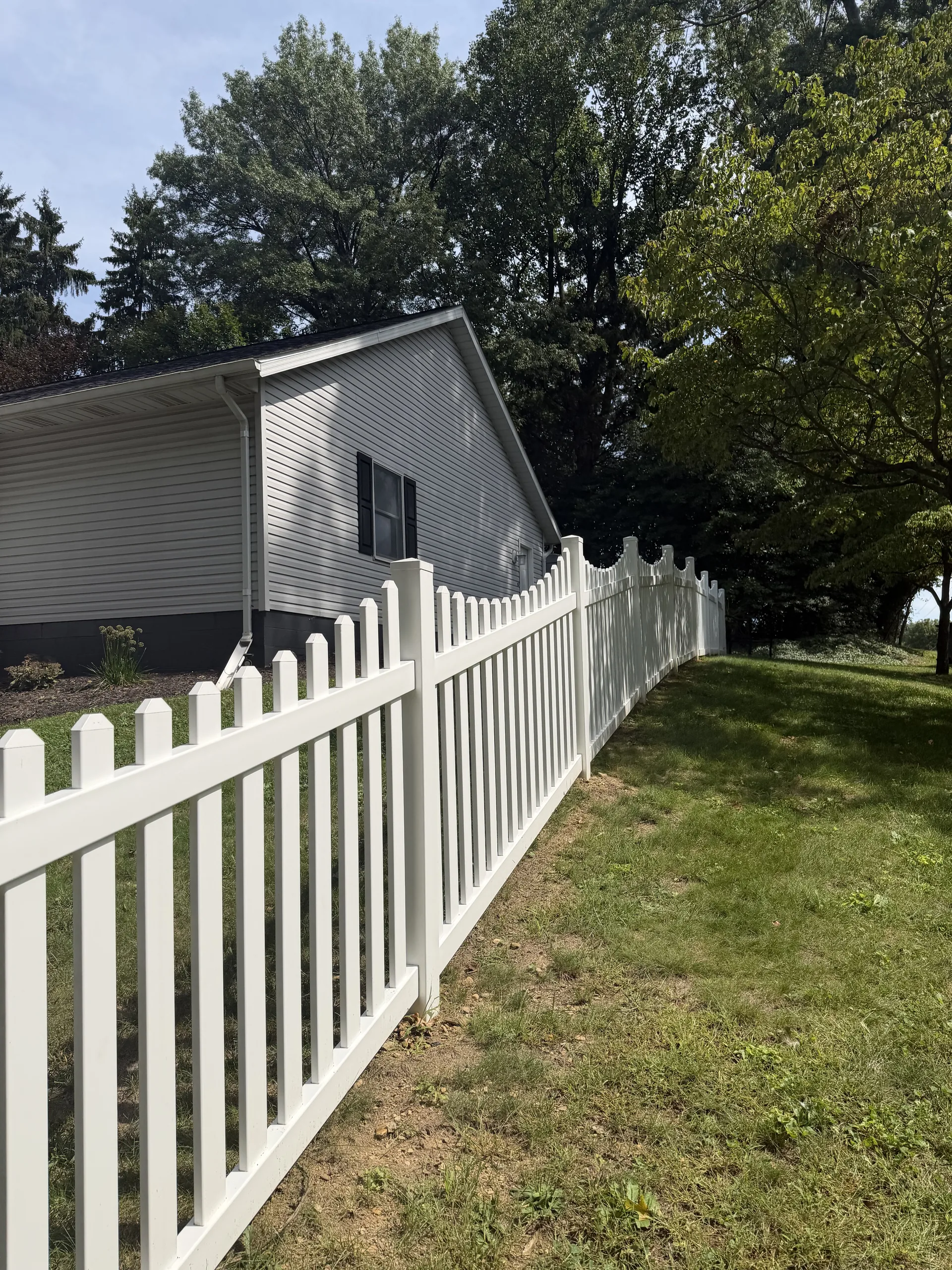 White picket fence following the slope of a lawn beside a gray house