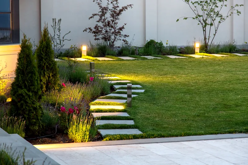 Landscaped yard at dusk with lit stepping stones and low planting