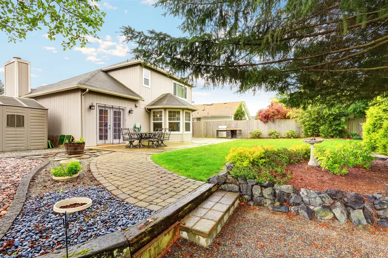 Backyard with a paver patio, stone retaining wall and planted borders