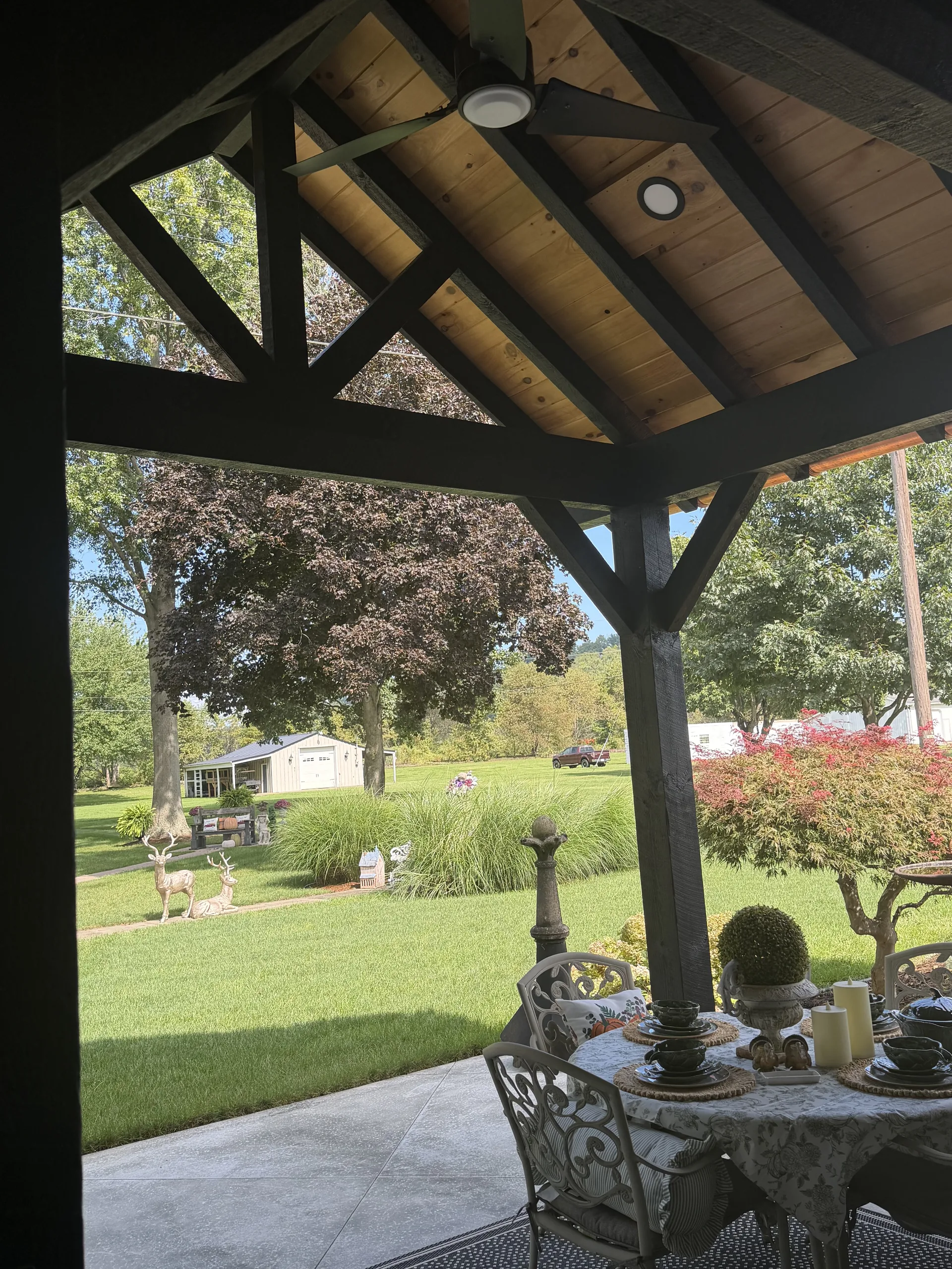 View from under the pavilion past a set dining table to the lawn, framed by black timber posts