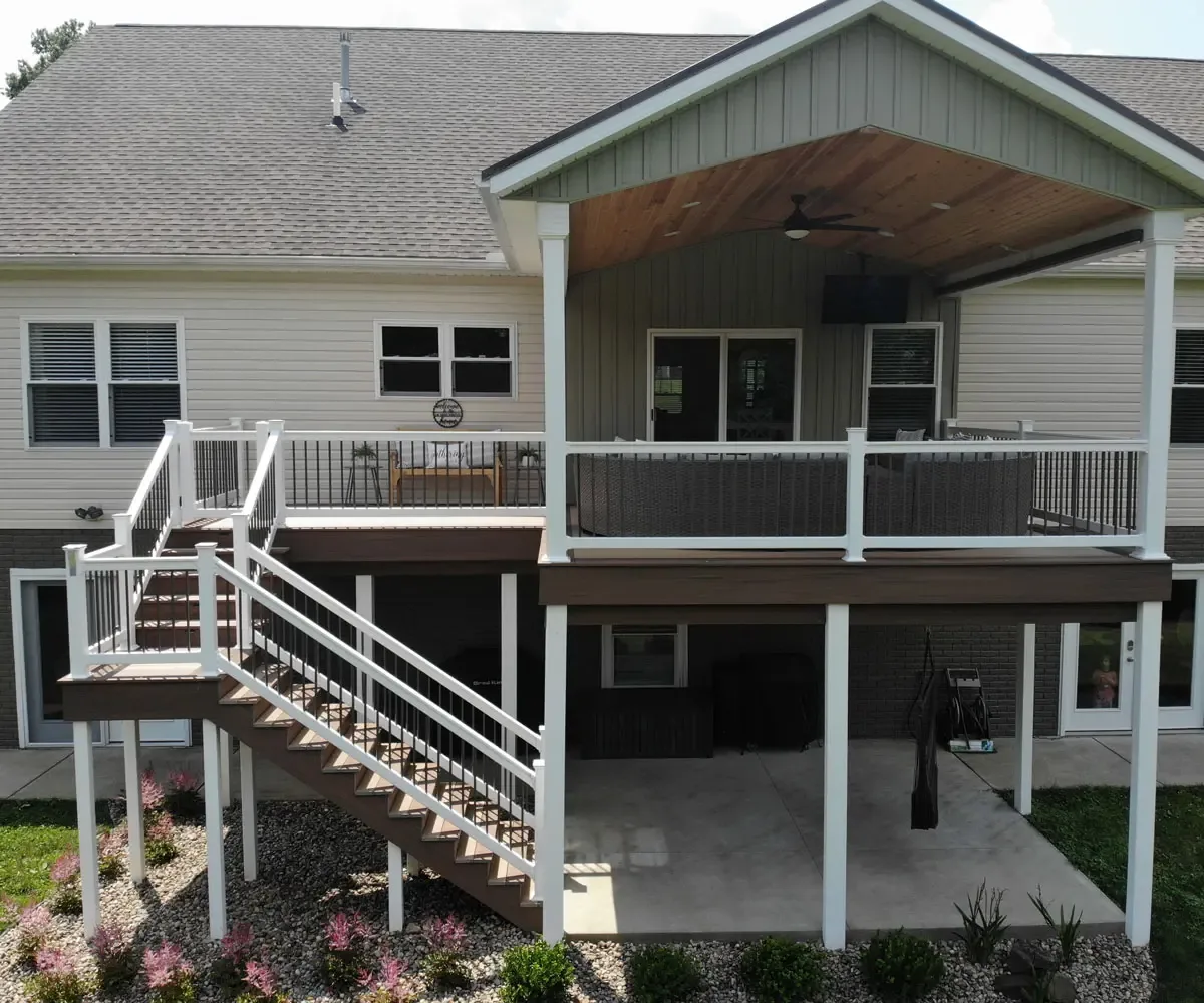 Two-storey home with a covered deck, white railing and stairs down to a patio