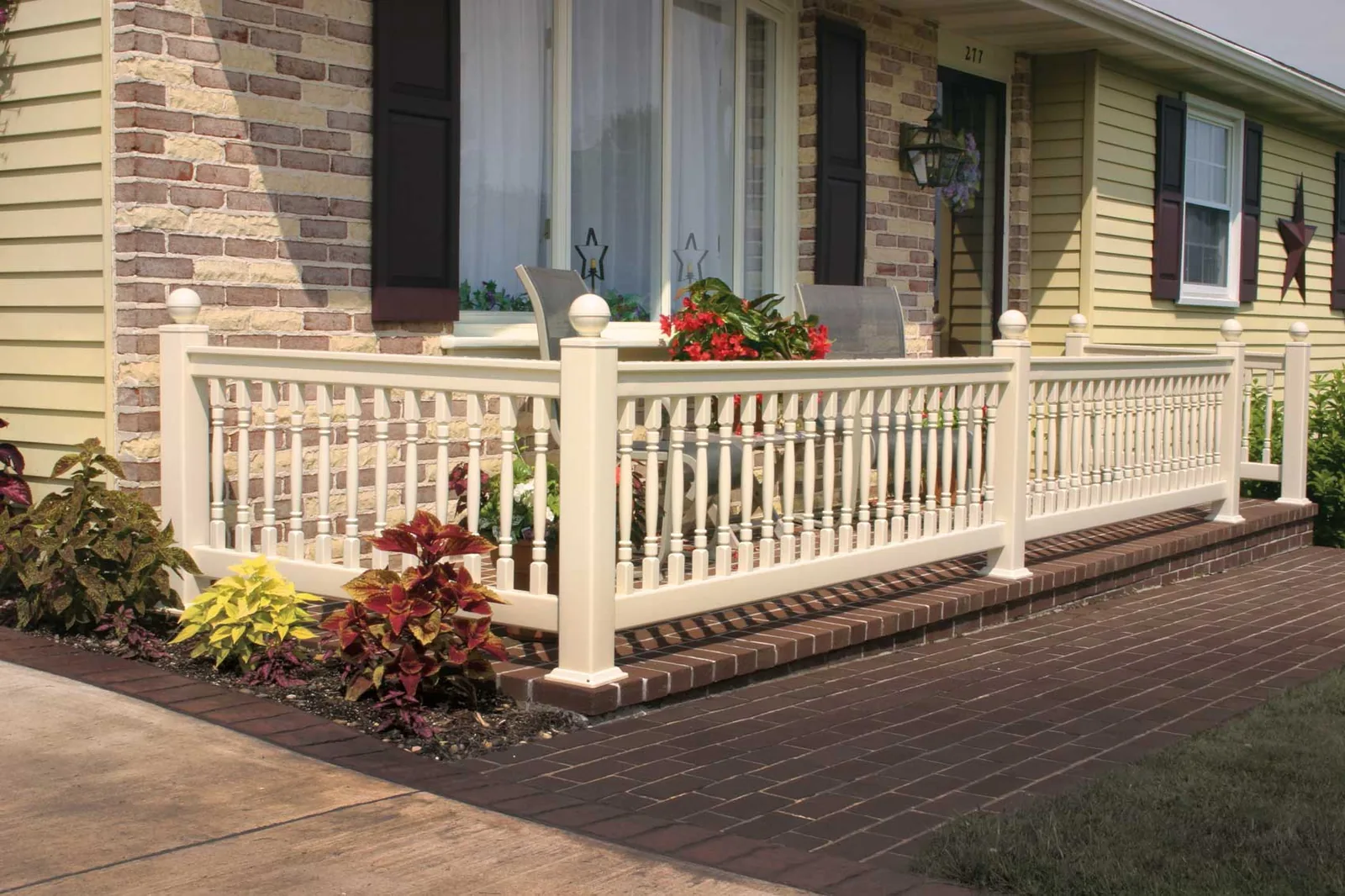 White vinyl porch railing on a brick and vinyl-sided home with planted borders