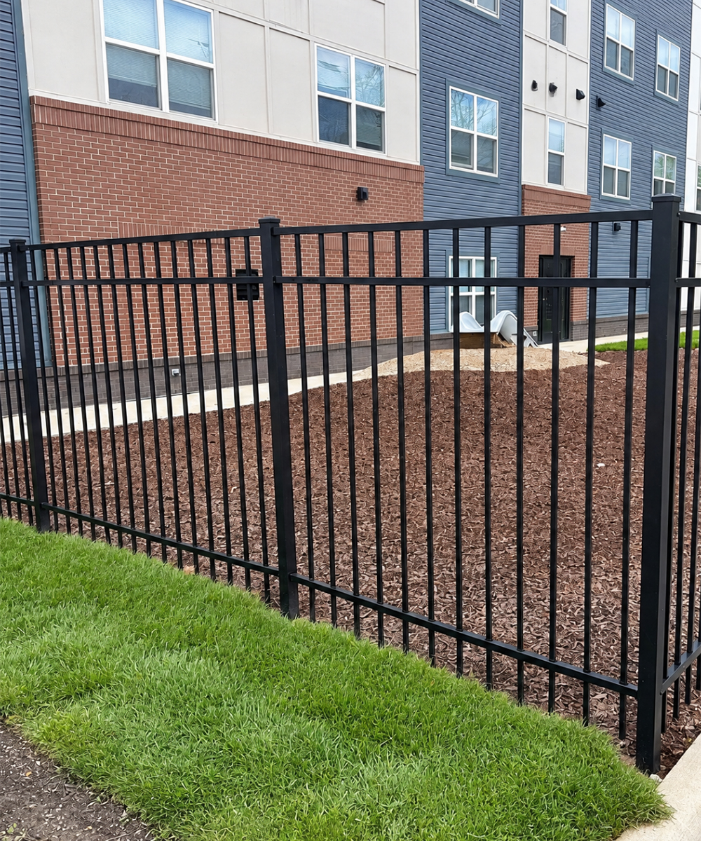 Black metal fence enclosing a landscaped area beside an apartment building