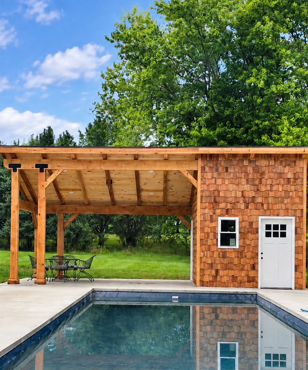 Cedar-shingled pool house with an attached timber pavilion beside an in-ground swimming pool
